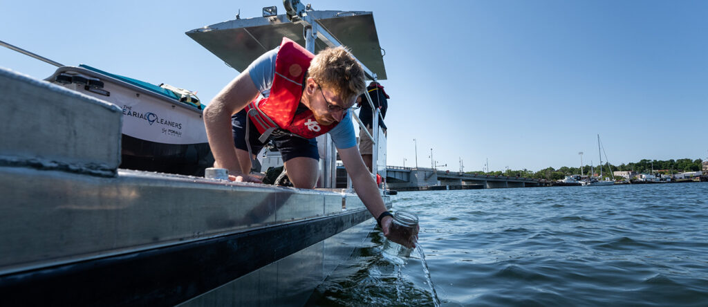 UWO student Mason Kobilic from Oakfield WII, takes a water sample to examine microplastics in the waters of Sturgeon Bay.